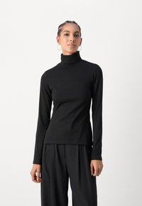 Must valge pikkade varrukatega turtleneck, mis on valmistatud pehmest kangast ja on lähedalt järgnev disain. Sile tekstuur lihtsa silueti ja ilma nähtavate mustrite või detailideta.