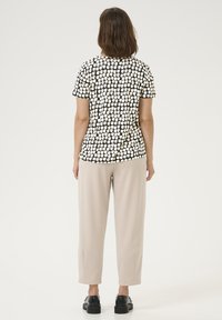 T-shirt a righe bianco e nero con maniche corte, abbinato a pantaloni beige chiaro e scarpe nere. Il tessuto sembra morbido con una consistenza liscia.