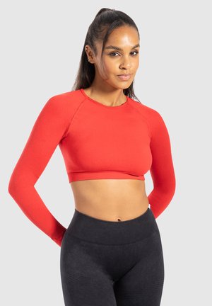 Rød cropped langærmet top med rund hals, lavet af et glat stof, parret med højtaljede sorte leggings med et struktureret mønster.