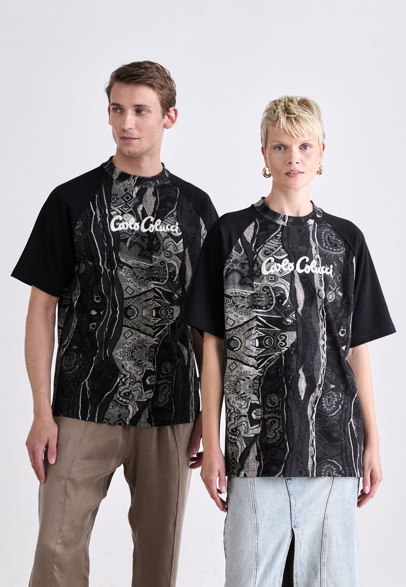 Sorte og mønstrede oversized t-shirts med abstrakte designs i grå og hvid, med et synligt logo i midten.
