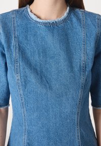 Denim-kjole med korte ermer, lyseblå farge, med en frynset halslinning og kontrasterende sømmer langs sømmene.