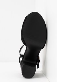 Sandale noire à fines lanières avec semelle texturée et talon bas et épais, vue de dessous sur fond blanc.
