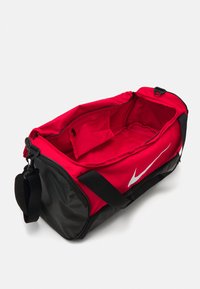 Rode sporttas met zwarte onderkant, voorzien van een groot wit logo, een ritsvak aan de binnenkant en dubbele zwarte handvatten om te dragen.