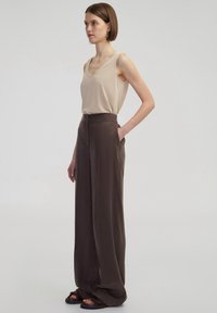 Béžový top bez rukávů s výstřihem do V, kombinovaný s hnědými širokými kalhotami s vysokým pasem, které mají boční kapsy a hladkou strukturu.