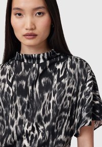 Top de estampado animal en blanco y negro con cuello alto y mangas cortas, que presenta una tela ligera y una textura suave.