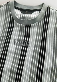 Camiseta a rayas en negro y gris con textura acanalada y un logo bordado "VENEZIA" en el frente. Presenta un cuello redondo gris de contraste.