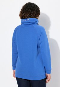 Blå tröja med hög krage och dragsko. Tillverkad av mjukt tyg, har ribbade ärmslut och en lös passform.
