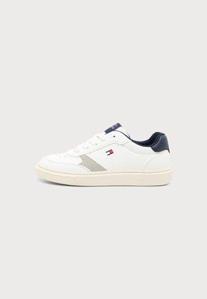 Λευκό sneaker χαμηλού ύψους με σκούρο μπλε φτέρνα, μπεζ σόλα, γκρι λεπτομέρεια στο πλάι και μικρό λογότυπο με κόκκινη, λευκή και μπλε σημαία στη πλευρά.