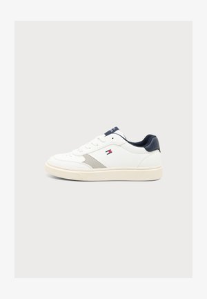 Baskets basses blanches avec talon bleu marine, semelle beige, détail latéral gris et petit logo drapeau rouge, blanc et bleu sur le côté.