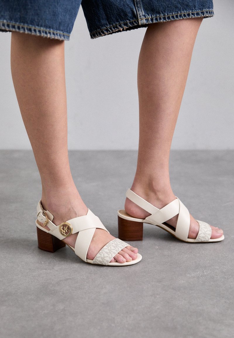 Beige hakken sandalen met kruislings banden, textuur op het voorpaneel en gouden hardware. Voorzien van een houten hak en een open te ontwerp.