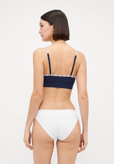 Bralette blu navy con spalline sottili regolabili e fascia con logo bianco. Abbinato a slip bikini bianchi semplici. Tessuto liscio e elasticizzato.