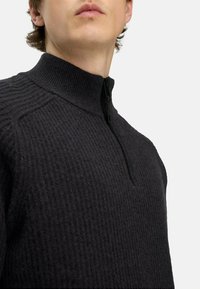 Schwarzer Zip-Hals-Pullover mit strukturiertem Rippenmuster. Verfügt über einen hohen Kragen und minimale Nähte für einen modernen, geschliffenen Look.