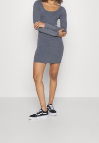 Grå långärmad ribbad klänning med rundad hals, figurnära design, kombinerad med svart och vita sneakers med snörning och kontrasterande detaljer.