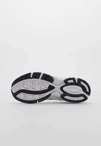 Semelle d'une chaussure de sport blanche et noire montrée sur un fond uni gris clair.