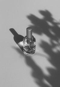 Clear glass perfume bottle with a silver screw-on cap, featuring a minimalist label design and casting a soft shadow on a light surface.