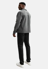 Chaqueta de forro polar gris con cuello, que presenta una textura suave y bolsillos delanteros, combinada con pantalones negros y zapatillas blancas.