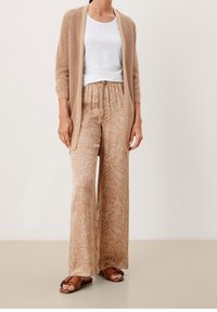 Beige stickad cardigan över en vit topp, parat med ljusa, vida byxor med ett bladmönster. Bruna sandaler fulländar looken.