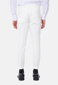 Pantaloni bianchi su misura con una vestibilità slim, dotati di tasche posteriori e orlo arrotolato, abbinati a scarpe e calze nere.