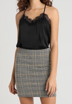 Woman wearing a black lace-trimmed cami top tucked into a high-waisted, knee-length plaid skirt with black, white, and beige colors.