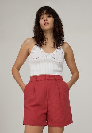 Top corto bianco lavorato a maglia con scollo rotondo, abbinato a pantaloni corti rossi in lino a vita alta con tasche laterali e fronte plissettato.