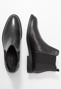 Botas de tobillo de cuero negro con acentos laterales elásticos, un diseño elegante y punta redonda, con costuras sutiles y una suela texturizada.