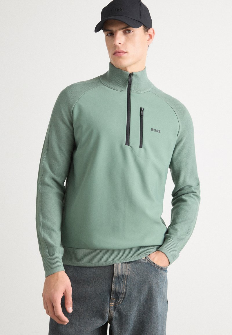 Minzgrüner Zip-Up-Pullover mit hohem Kragen und schwarzem Reißverschluss. Taillierte Bündchen und Saum mit Rippstrick. Mit subtiler Markenplatzierung auf der Brust.