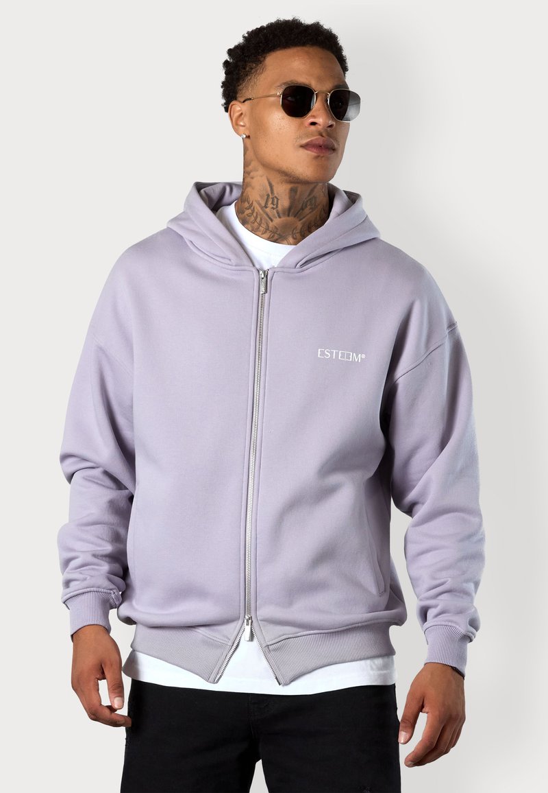 Light purple hooded sweatshirt with front zipper, ribbed cuffs and hem, featuring a white logo on the chest, layered over a white shirt.