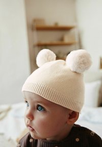 Cappello lavorato a maglia beige chiaro con due pompon soffici in cima. Presenta un orlo a coste e un motivo testurizzato.