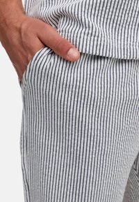 Pantalones a rayas fabricados con tejido ligero; presentan rayas verticales en azul marino y blanco, superficie texturizada y detalles de bolsillos laterales.