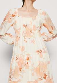 Kremowa sukienka midi w kwiaty z pomarańczowo-brzoskwiniowymi wzorami, prostokątnym dekoltem, długimi bufkami oraz marszczonym wcięciem w talii z warstwowym krojem.