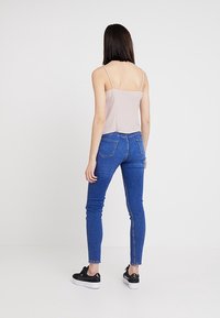 Hellgraues Spaghettiträgershirt kombiniert mit blauen Skinny Jeans, die eine hohe Taille, Taschen hinten und schwarze Sneaker mit weißer Sohle haben.