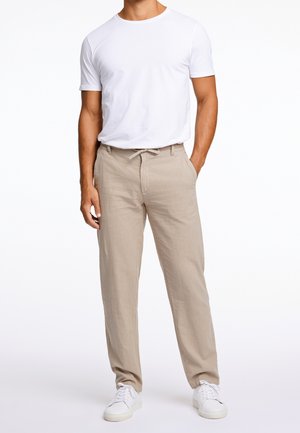 Valkoinen lyhythihainen t-paita yhdistettynä vaaleanbeigeihin pellavahousuihin, joissa on joustava vyötärö. Täydennä rentoon asuun valkoisilla tennareilla.