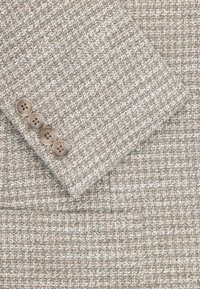 Rękaw beżowo-brązowej marynarki w pepitkę z czterema brązowymi guzikami, spoczywający na dopasowanej, teksturowanej tkaninie.