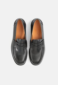 Svarta läderloafers med en slät yta, en dekorativ rem och sömnadsdetaljer. Inredningen har en brun läderfoder.