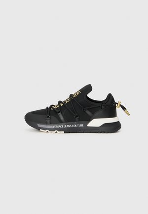 Basket noire Versace Jeans Couture avec logo doré sur la languette, détail blanc sur la semelle, lacets élastiques et languette à embout doré au talon.