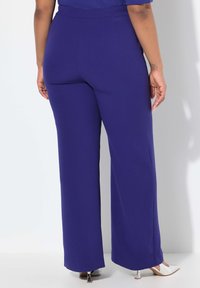 Pantalones de pierna ancha en color púrpura con una cintura elástica. Tela suave y elástica. El dobladillo es ligeramente acampanado, terminando justo por encima de los zapatos.