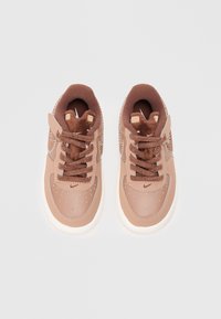 Barna színű edzőcipő sima bőr felsőrésszel, barna fűzőkkel és finom perforációkkal. Fehér gumitalp és texturált barna nyelv.