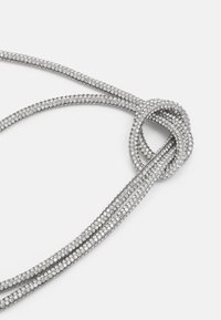 Sølv halskjede bestående av sammenvevde tråder, prydet med små rhinestones, med en sentral knute-detalj og en glatt overflate.