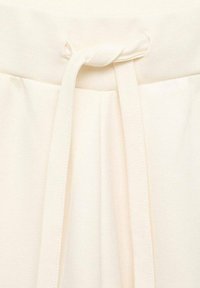 Cinturilla de tela color crema con cordón atado. Tela tejida texturizada con pliegues a ambos lados, detalle mínimo de costura.