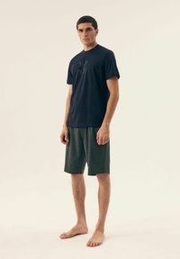 Granatowy t-shirt z nadrukowanym hasłem na piersi, zestawiony z zielonymi szortami w wzory. Oba elementy są lekkimi, casualowymi ubraniami do relaksu.