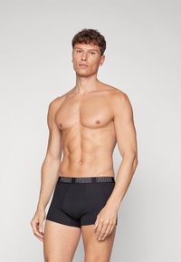 Schwarze Baumwoll-Boxershorts mit einem breiten elastischen Bund, der das Puma-Logo in Weiß zeigt. Die Passform ist eng und die Textur erscheint glatt.
