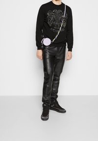 Svart sweatshirt med strassdetaljer och texten "RICH", i kombination med tajta svarta läderbyxor. Modellen bär en rund lila väska med ett mönstrat band.