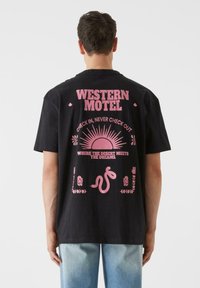 Must teemant T-särk lühikeste varrukatega, millel on roosa graafiline print, sealhulgas tekst "WESTERN MOTEL" ja kõrbemotiivid seljal. Igapäevane lõige.