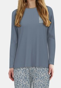Lichtblauw langemouwen top met een ronde hals en een textuurlagige afwerking, gecombineerd met patroon lichtblauwe en beige broek met abstracte vormen.