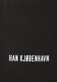 Borsa tote nera in tela con testo bianco audace che recita "HAN KJØBENHAVN" in lettere maiuscole, enfatizzando un design minimalista.