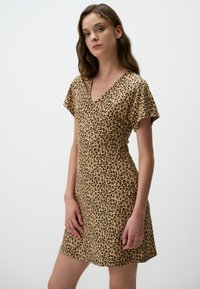 Leopardprintjurk in lichtbruin met korte mouwen en een v-hals ontwerp. Gladde textuur, gemiddelde bovenbeenlengte, getailleerde pasvorm.