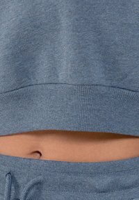 Felpa blu cropped con orlo a coste, abbinata a pantaloni jogger coordinati. Il tessuto sembra morbido, con una leggera texture.