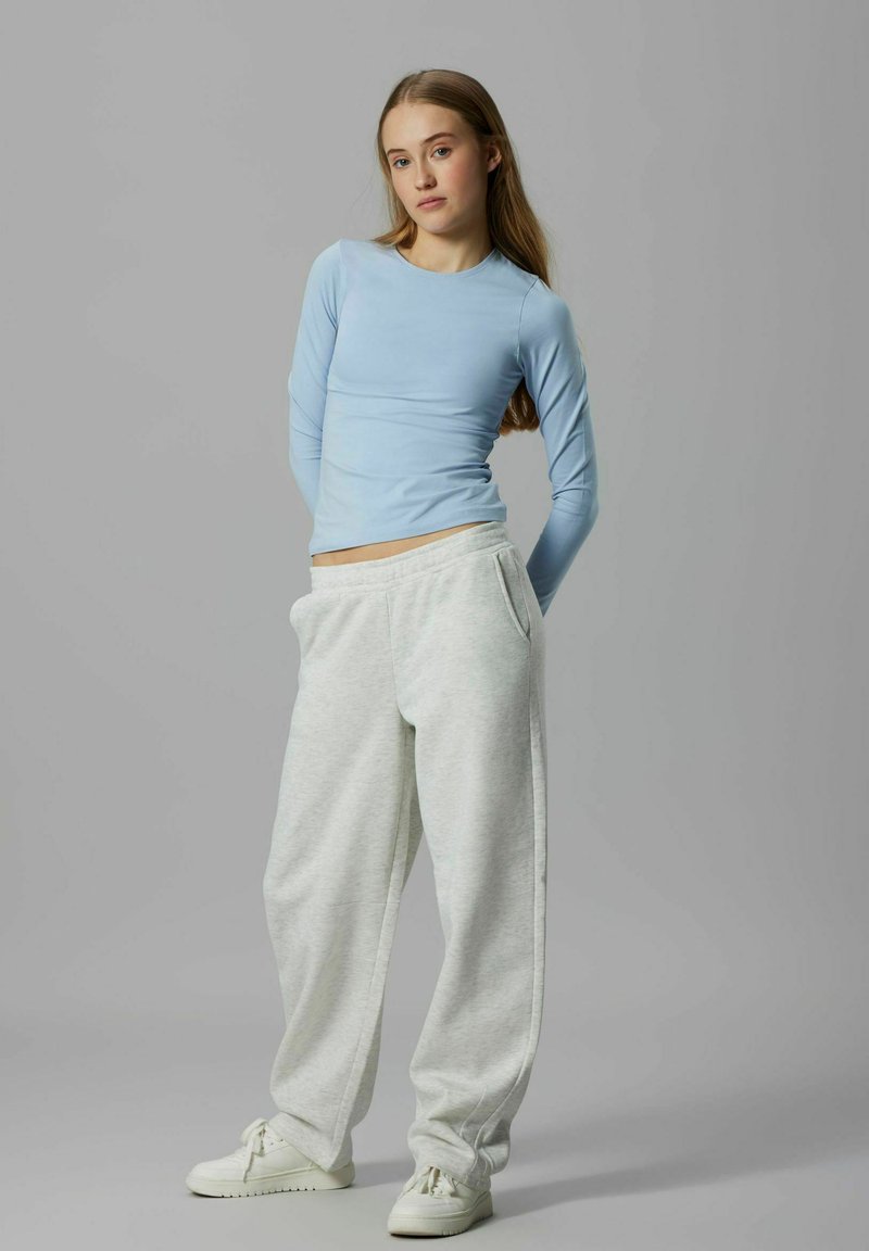 Helehelesinine pika varrukaga särk ümmarguse kaelusega, kombineeritud lahtiste hallide dressipükstega ja valgete tossudega. Lihtne disain ja pehme kangas.