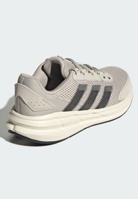 Light gray athletic shoe with mesh upper, three dark gray stripes, cushioned sole, and textured heel detail.