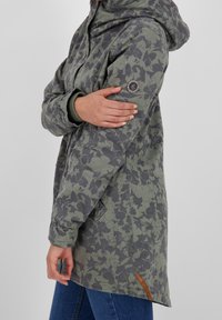 Chaqueta verde con estampado floral y capucha, que presenta mangas largas, un zipper y un detalle marrón en el dobladillo. Hecha de un tejido ligero y texturizado.